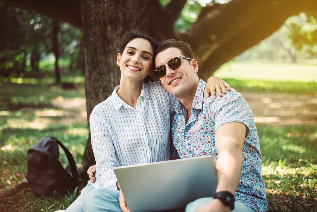 Пара молодий підліток коханець сидить і використовує ноутбук комп'ютер разом в парку, романтичний і насолоджується в момент часу щастя, щасливий і усміхнений
 - Фото, зображення