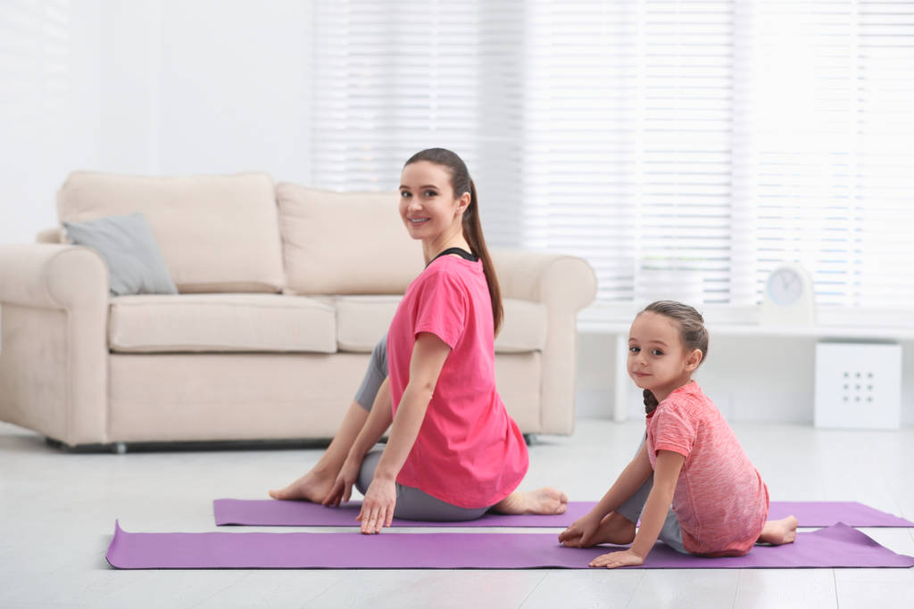 Junge Mutter mit kleiner Tochter praktiziert Yoga zu Hause - Foto, Bild