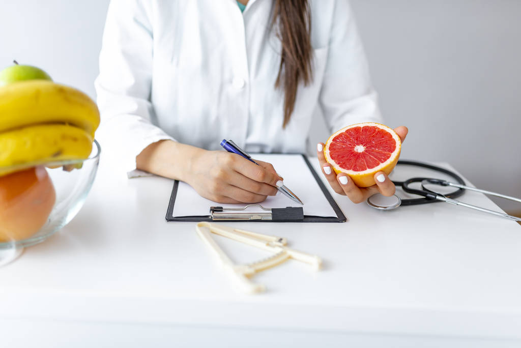 栄養士は、患者のための食事計画を書いてパノラマ、コピースペース。彼女の机で働いている果物と女性栄養士。栄養士は食事計画に取り組んでいます。減量と右栄養の概念 - 写真・画像