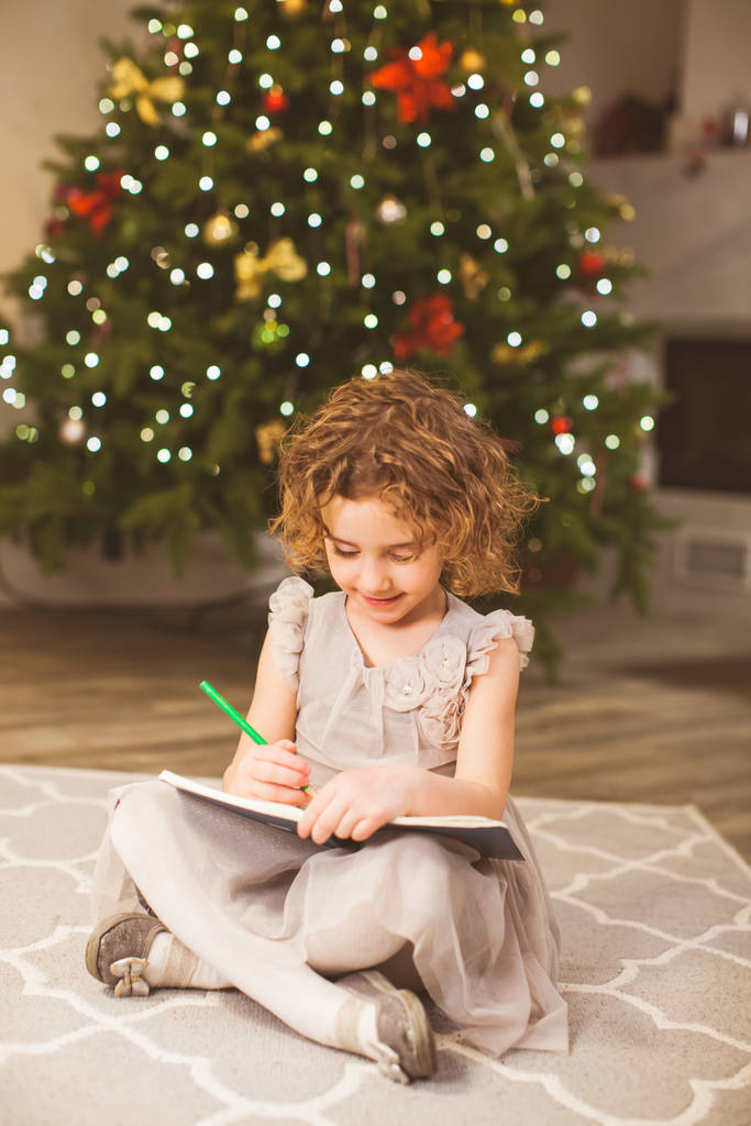 chica escribe carta a santa cerca de árbol de Navidad
 - Foto, Imagen