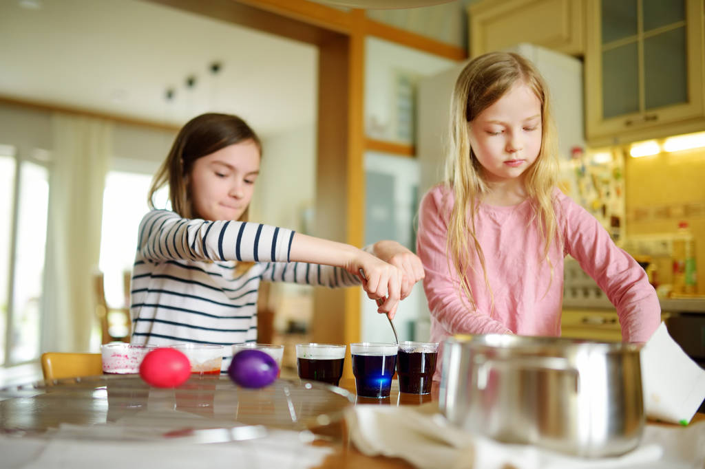 自宅のイースターエッグを染色 2 つかわいい若い姉妹。子供たちはイースター ハントのカラフルな卵を塗るします。子供たちはイースターのお祝いの準備を。家族の伝統. - 写真・画像