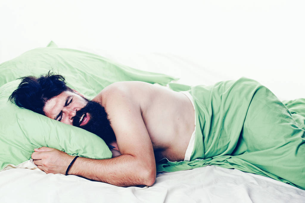 Νεαρός κοιμάται σε μαλακά μαξιλάρια στο κρεβάτι στο σπίτι. Το να κοιμάσαι σαν άντρας. Ο άνθρωπος κοιμάται στο μαξιλάρι στο κρεβάτι στο σπίτι. - Φωτογραφία, εικόνα