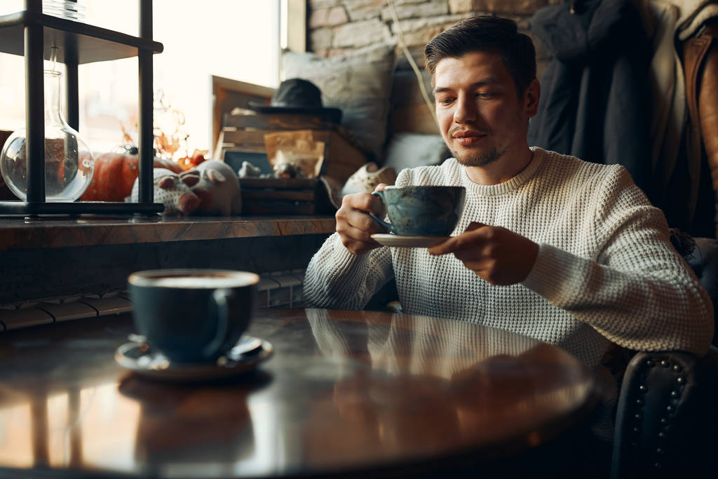 σοβαρός ελκυστικός άντρας σε κομψό λευκό πουλόβερ κρατώντας ένα φλιτζάνι τσάι - Φωτογραφία, εικόνα