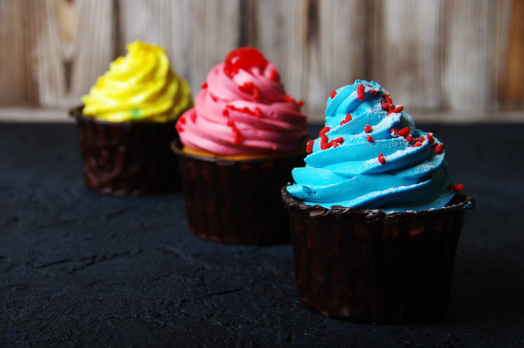 Cupcake cakes geel, roze, blauw op een donkere achtergrond - Foto, afbeelding