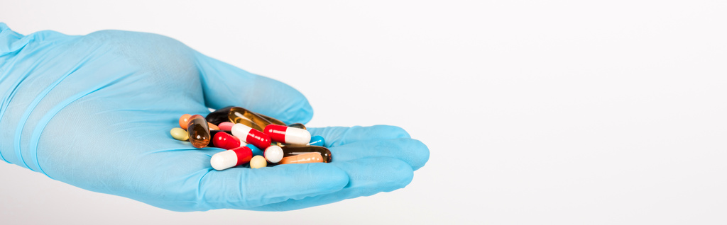 tiro panorâmico do cientista na luva de látex azul segurando pílulas isoladas no branco
  - Foto, Imagem