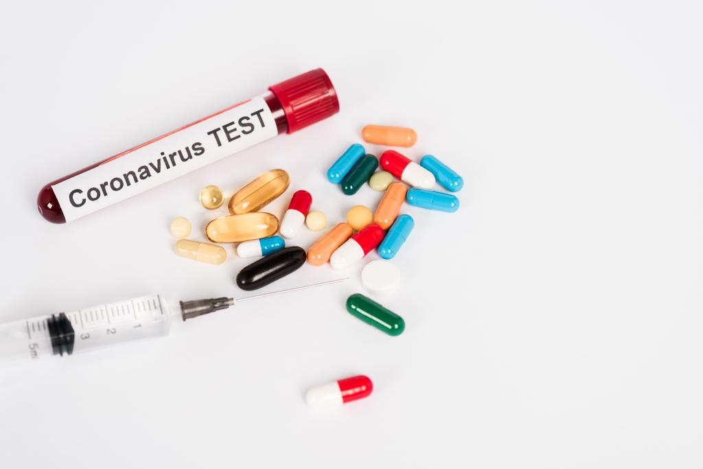 πολύχρωμα χάπια κοντά στο δείγμα με γράμματα δοκιμής coronavirus και σύριγγα σε λευκό  - Φωτογραφία, εικόνα