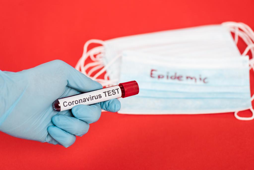 vue recadrée d'un scientifique tenant un échantillon avec inscription du test du coronavirus près de masques médicaux isolés sur du rouge
  - Photo, image