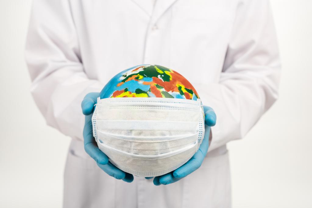 обрезанный вид ученого держащего земной шар в защитной маске изолированный на белом
  - Фото, изображение