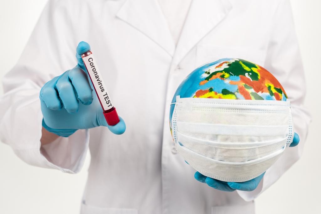 καλλιεργημένη άποψη του επιστήμονα που κρατά τη σφαίρα με προστατευτική μάσκα και δείγμα με γράμματα δοκιμής coronavirus που απομονώνονται σε λευκό  - Φωτογραφία, εικόνα