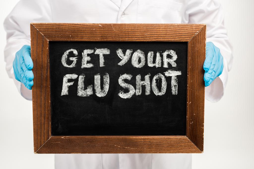 vista cortada do cientista em luvas de látex segurando quadro-negro com obter o seu tiro gripe lettering isolado no branco
  - Foto, Imagem