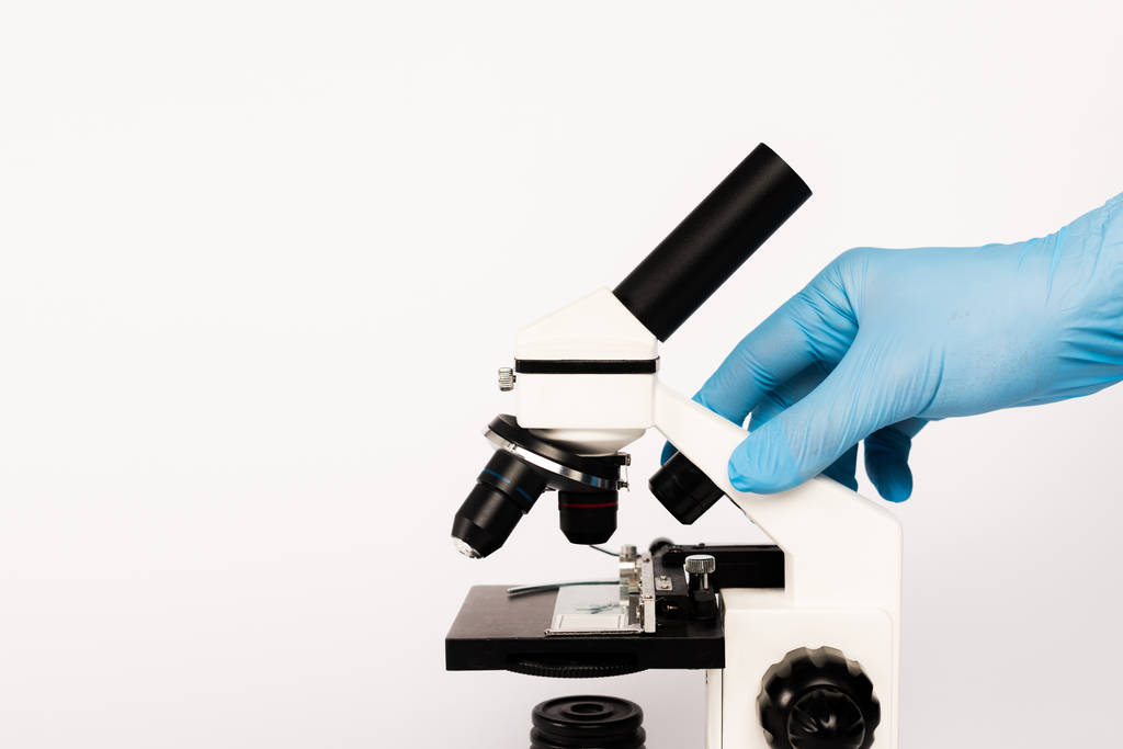 oříznutý pohled vědce v latexové rukavici dotýkající se mikroskopu izolovaného na bílém  - Fotografie, Obrázek
