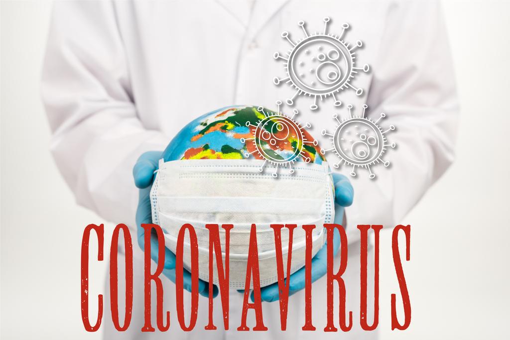 обрезанный вид ученого, держащего земной шар в защитной маске возле коронавируса с надписью на белом
  - Фото, изображение