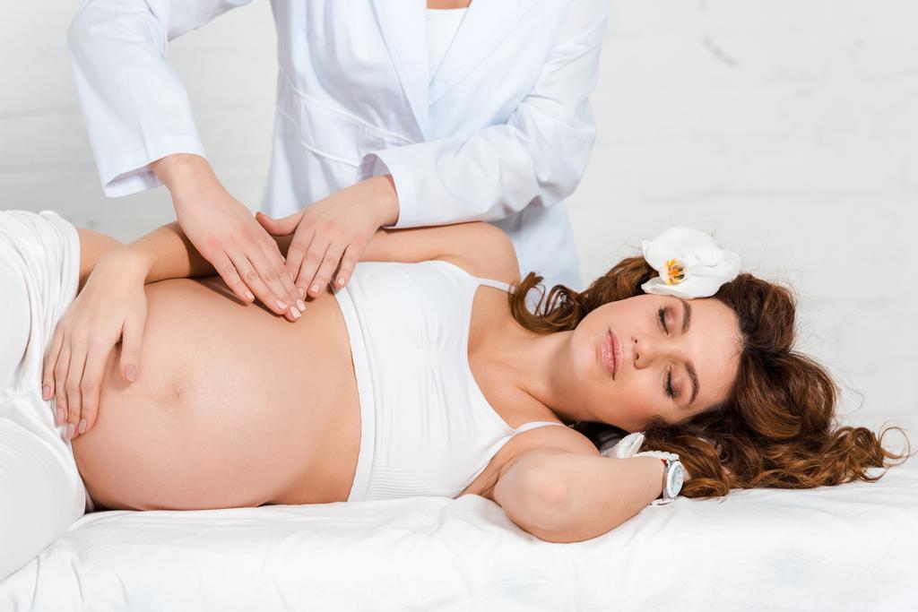 Masseur faisant le massage du ventre à la femme enceinte avec orchidée dans les cheveux dans le centre de spa
 - Photo, image