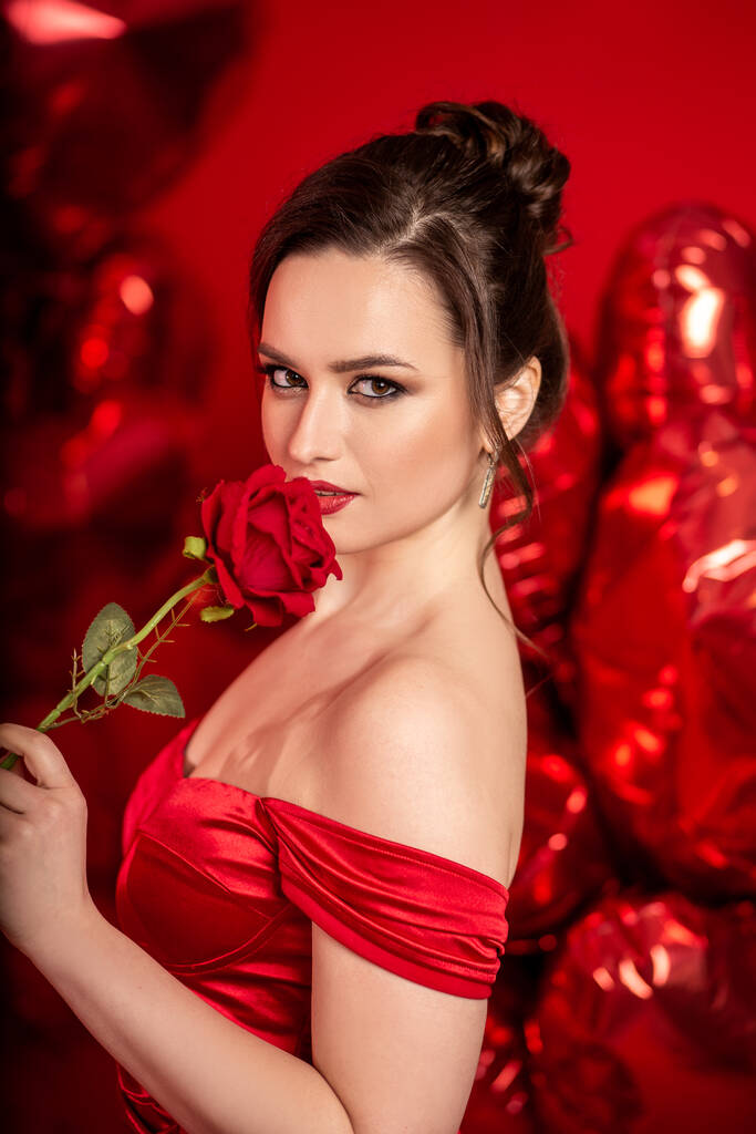 美しいです若いです若いです女性で赤夜ドレス上の赤い背景に大きなハート形の風船.  - 写真・画像