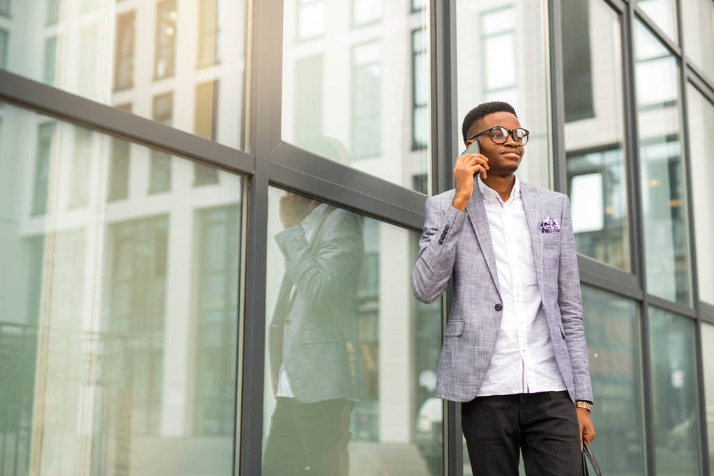 bel giovane africano in giacca e cravatta con un telefono in mano vicino a un edificio di vetro
 - Foto, immagini