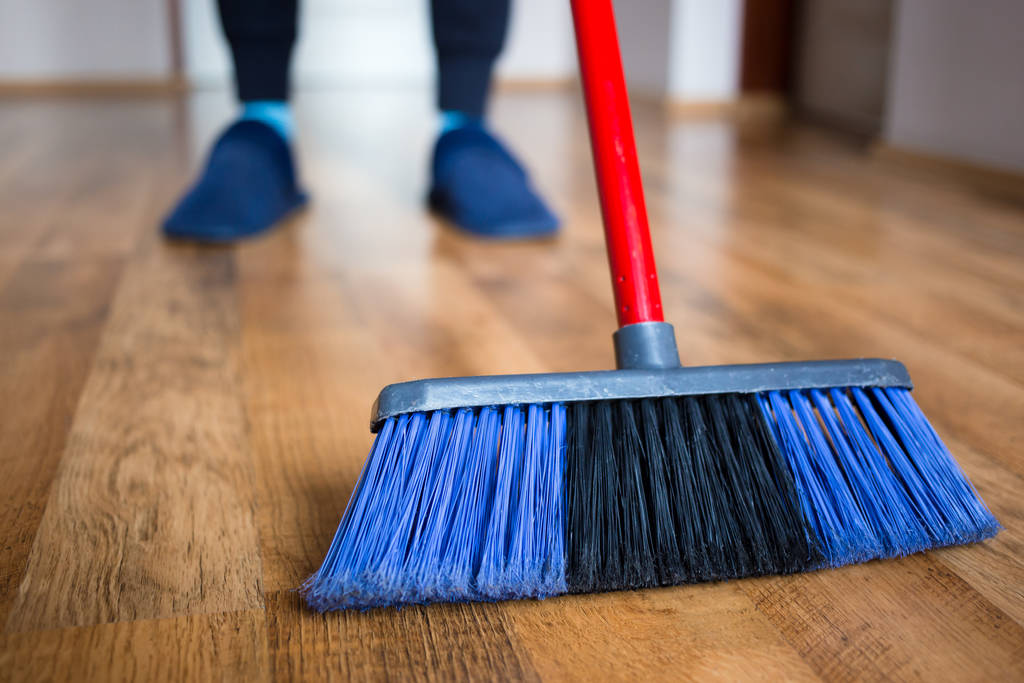 Manželka v modrých pantoflích používající vnitřní modré koště pro čištění podlah z tvrdého dřeva. - Fotografie, Obrázek