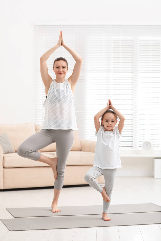 Madre joven con hija pequeña practicando yoga en casa
 - Foto, imagen