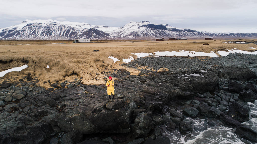 junger männlicher Reisender in grüner Kleidung mit rotem Hut und grünem Rucksack geht vor dem Hintergrund der isländischen Berge den Pfad entlang - Foto, Bild