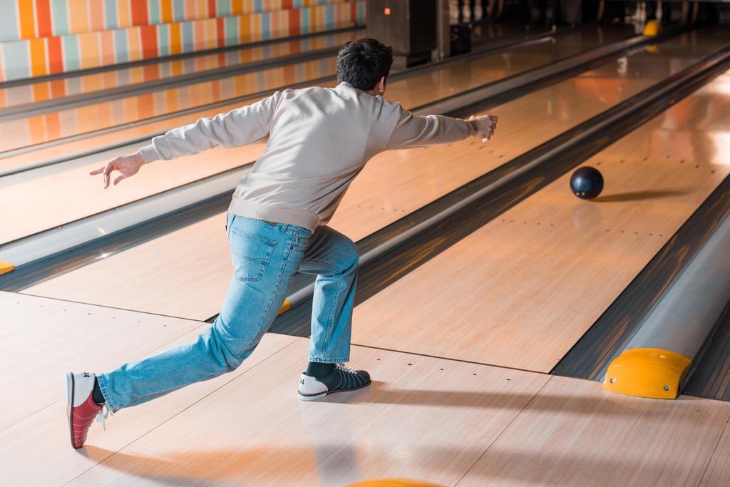 terug uitzicht op jonge man gooien bowling bal op kegelbaan - Foto, afbeelding