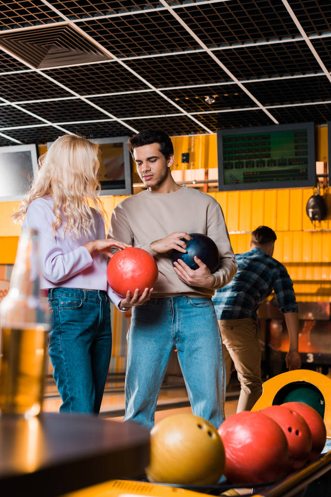 knappe man praten met blonde vriendin terwijl het vasthouden van bowling ballen - Foto, afbeelding
