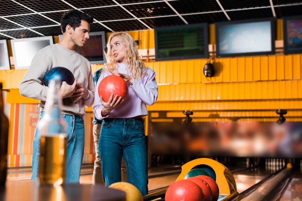 selectieve focus van jonge man en vrouw praten terwijl het houden van bowling ballen in bowling club - Foto, afbeelding