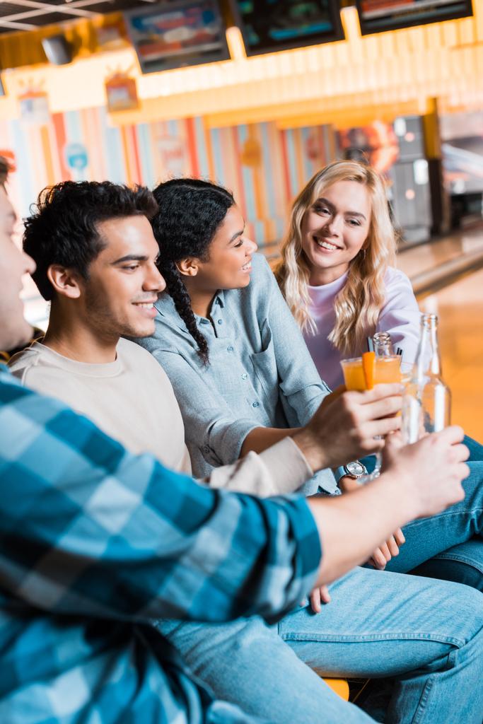 mosolygó multikulturális barátok kezében üveg sört és koktélpoharakat, miközben ül a bowling klub  - Fotó, kép