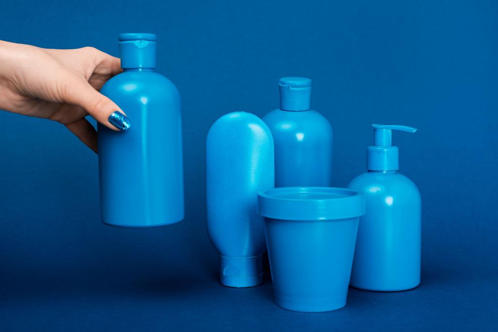 abgeschnittene Ansicht der Frau mit Flasche mit Shampoo auf blauem Hintergrund - Foto, Bild