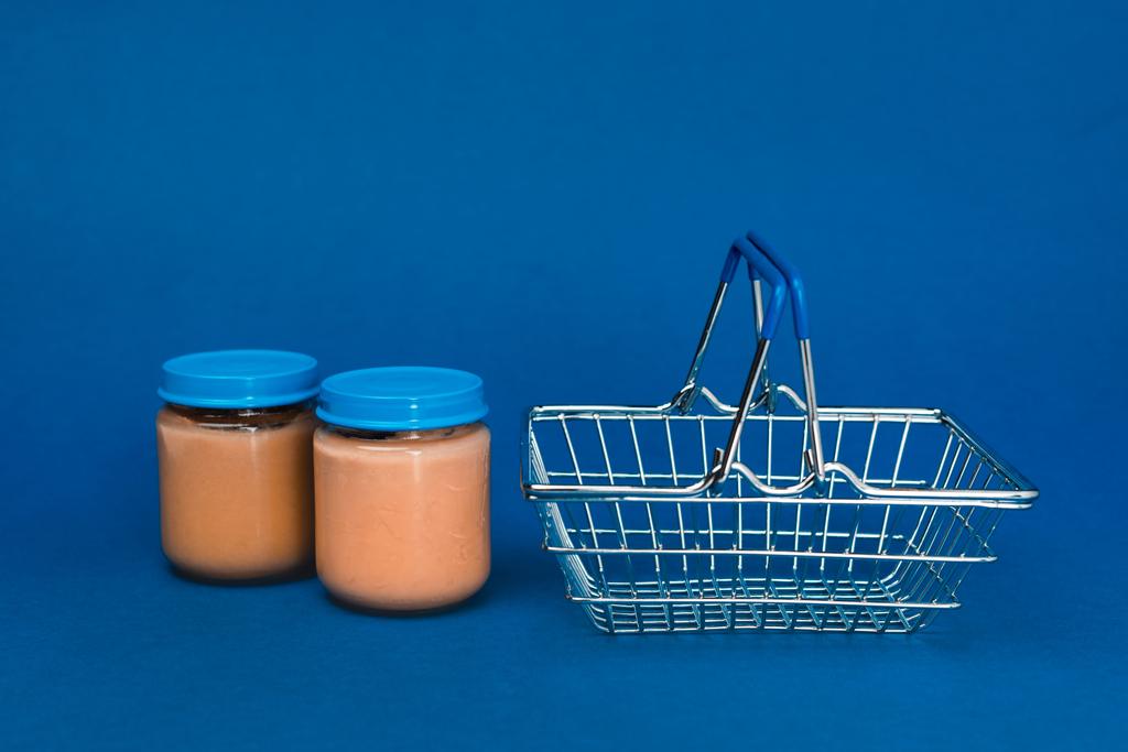 βάζα με παιδικές τροφές και καλάθι αγορών σε μπλε φόντο  - Φωτογραφία, εικόνα