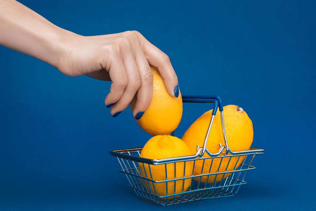 bijgesneden weergave van vrouw zetten citroen in winkelmandje op blauwe achtergrond  - Foto, afbeelding