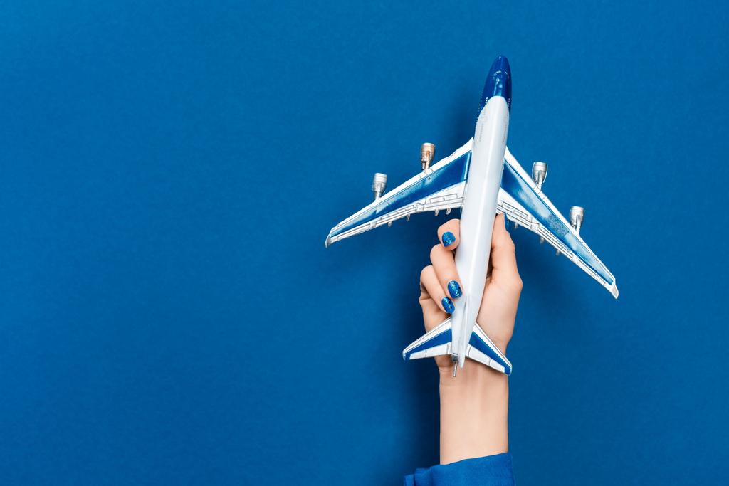 Ausgeschnittene Ansicht einer Frau mit Modell eines Flugzeugs auf blauem Hintergrund  - Foto, Bild