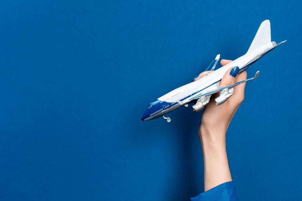 Ausgeschnittene Ansicht einer Frau mit Modell eines Flugzeugs auf blauem Hintergrund  - Foto, Bild