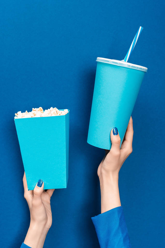 bijgesneden weergave van vrouw met popcorn en papier beker op blauwe achtergrond  - Foto, afbeelding