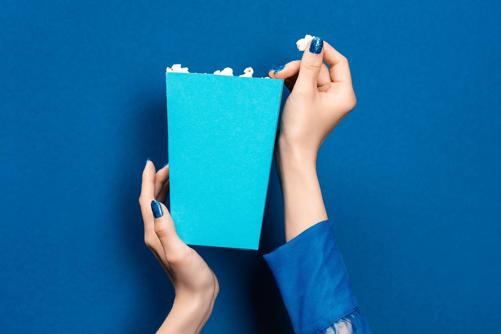 cropped view of woman holding box with popcorn on blue background  - Photo, Image