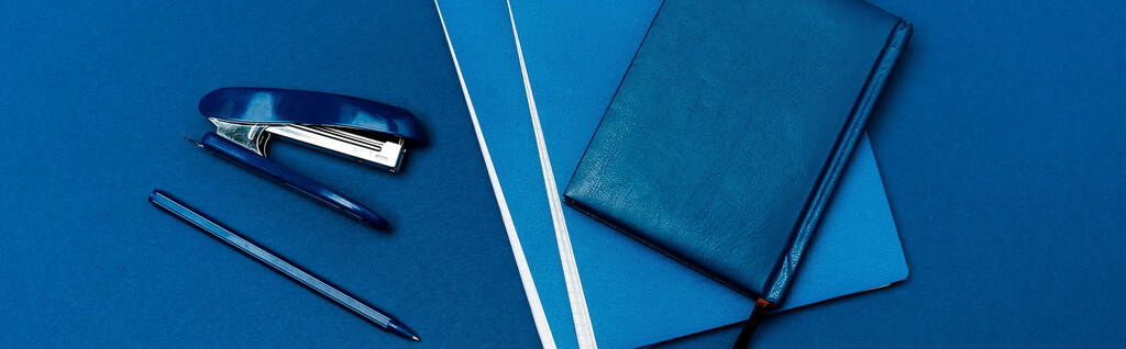 panoramic shot of notebooks, pen and stapler isolated on blue - Photo, Image
