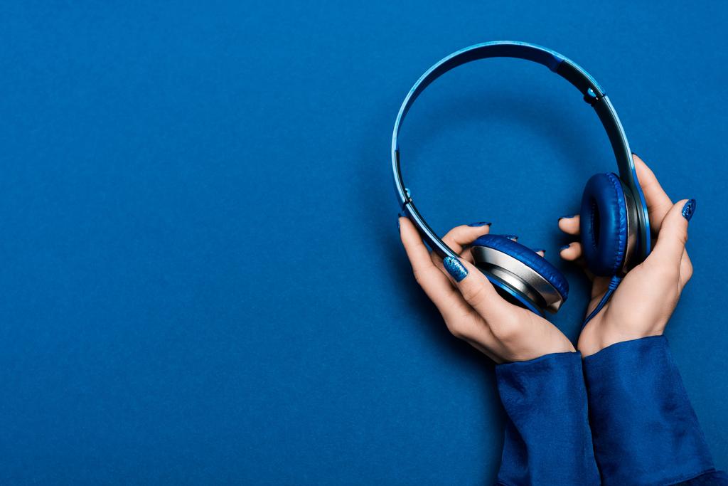 oříznutý pohled na ženu držící sluchátka na modrém pozadí  - Fotografie, Obrázek