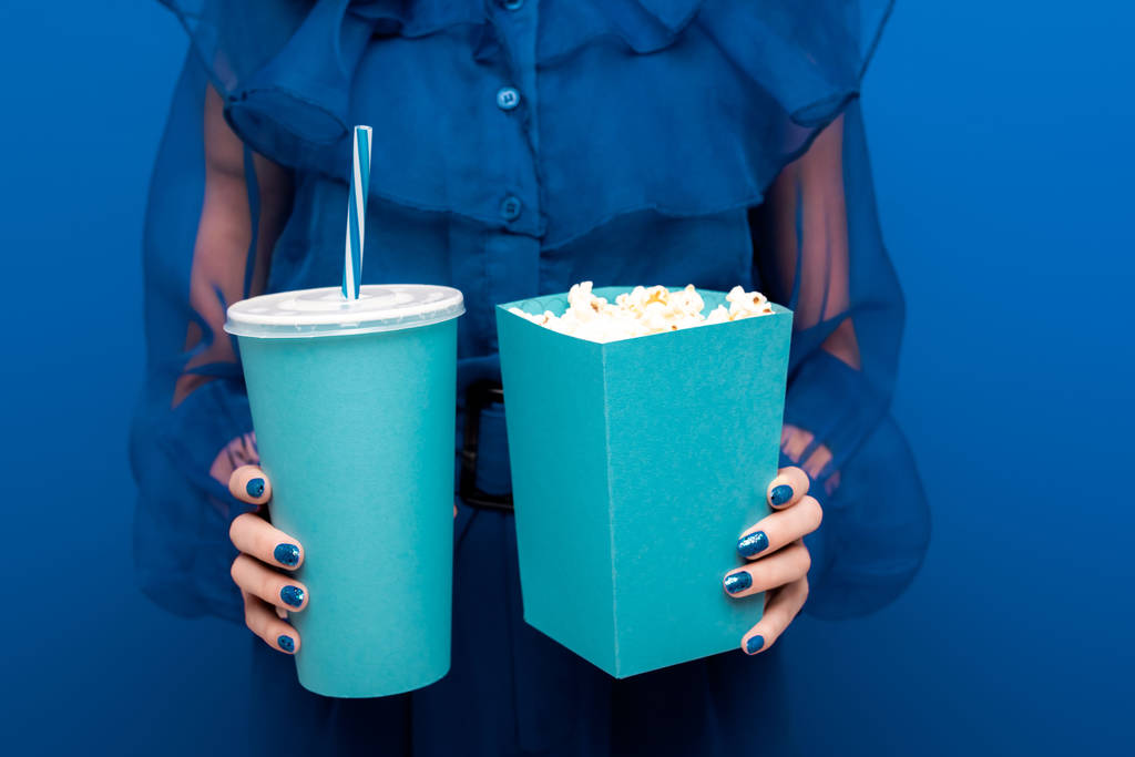 Ausgeschnittene Ansicht einer Frau mit Popcorn und Limo auf blauem Hintergrund  - Foto, Bild