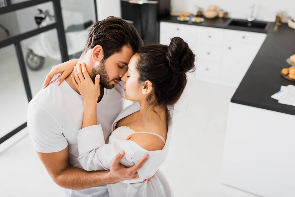 Mulher bonita em sutiã e camisa beijando namorado na cozinha
 - Foto, Imagem