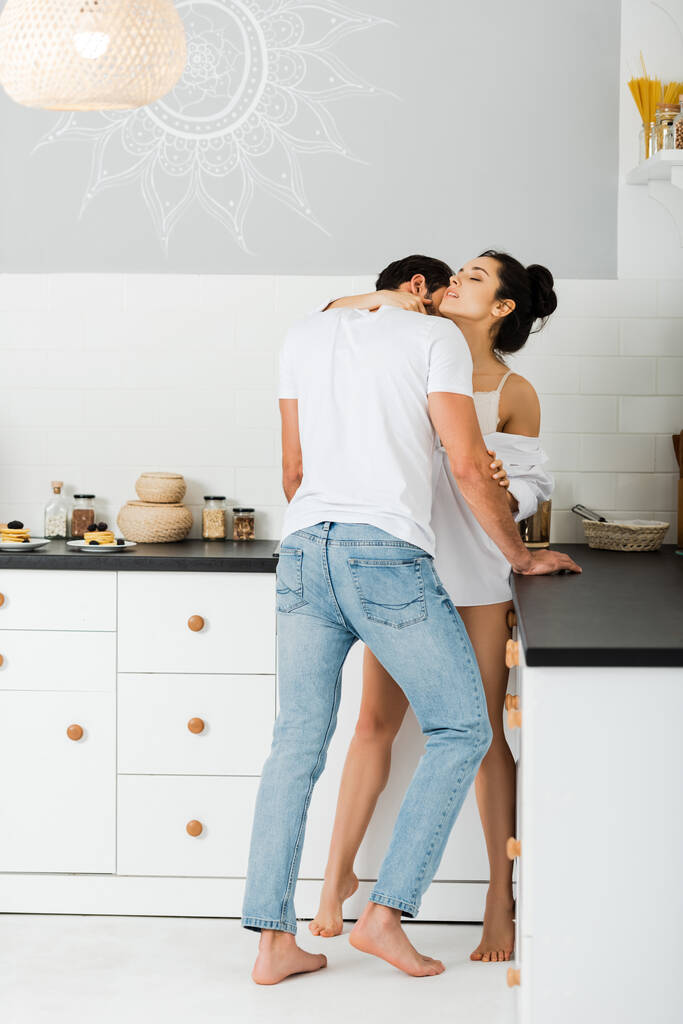 mężczyzna całowanie w szyję piękna kobieta w biustonosz i koszula w kuchni  - Zdjęcie, obraz