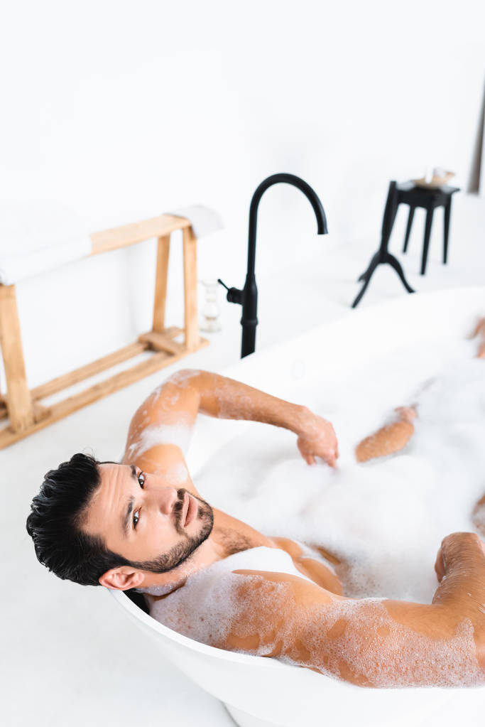 Wysoki kąt widzenia przystojnego mężczyzny patrzącego w kamerę podczas kąpieli w łazience - Zdjęcie, obraz