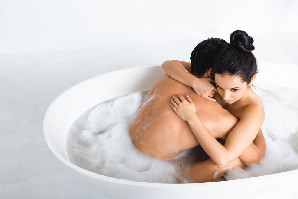 Όμορφη γυμνή γυναίκα αγκαλιάζει φίλο στην μπανιέρα με αφρό σε γκρι επιφάνεια σε λευκό φόντο - Φωτογραφία, εικόνα