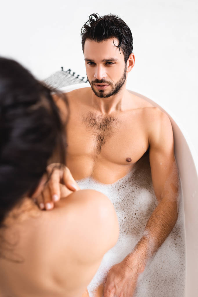 Szelektív fókusz jóképű izmos férfi nézi meztelen barátnő fürdőkád fehér háttér - Fotó, kép