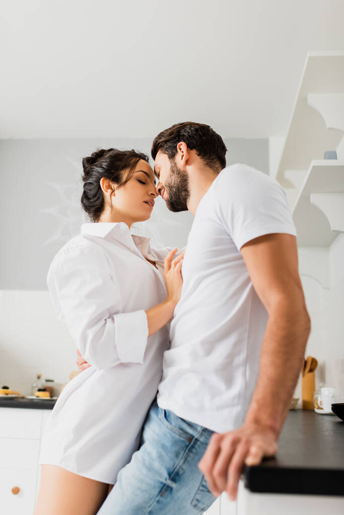 Vista laterale della ragazza sensuale in camicia baciare bel ragazzo vicino al piano di lavoro della cucina
 - Foto, immagini