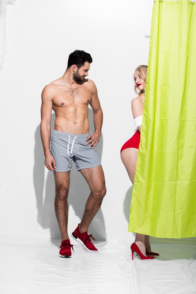 homem feliz olhando para nádegas de sedutor pin up menina de pé perto cortina de chuveiro no branco
  - Foto, Imagem