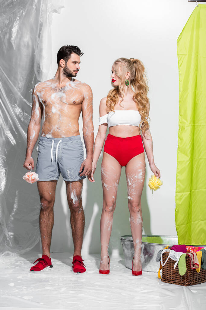 sexy pin up chica celebración de esponja húmeda con jabón cerca de hombre sin camisa en blanco
  - Foto, imagen
