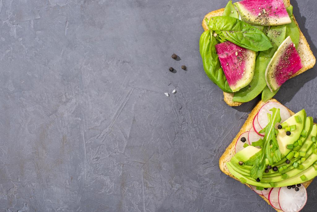 bovenaanzicht van gezonde vegetarische toast met radijs, avocado en basilicum - Foto, afbeelding