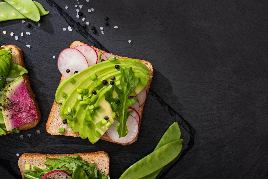 top view of organic sandwiches with radish and avocado on stone board with pepper and salt - Photo, Image