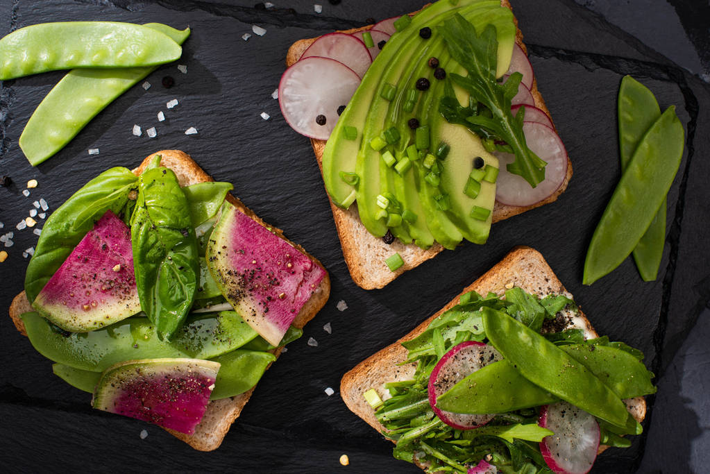 bovenaanzicht van gezonde toastjes met rauwe groenten met peper zaden en zout - Foto, afbeelding