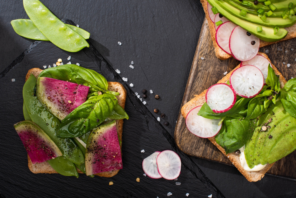 bovenaanzicht van gezonde toast met groenten op steen en houten planken met peper en zout - Foto, afbeelding