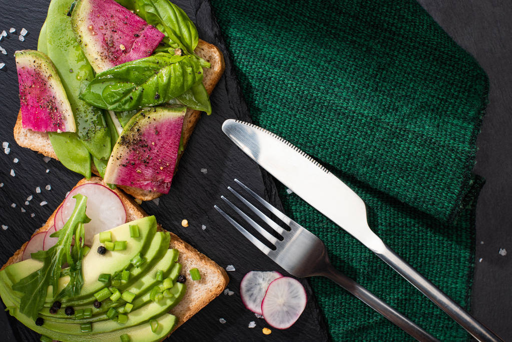 vista superior de sanduíches saudáveis com legumes frescos em pano com garfo e faca
 - Foto, Imagem