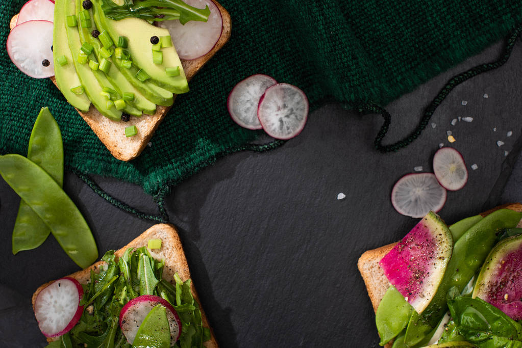 bovenaanzicht van verse broodjes met radijs, groenten en avocado op doek - Foto, afbeelding